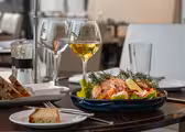 Et bord med en tallerken salat toppet med laks, citronskiver og dild, to glas hvidvin og en lille tallerken brød. Baggrunden har en moderne spisestue med blød belysning.